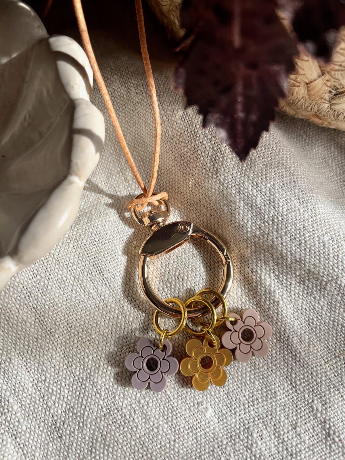Colorful flower charm keychain with gold and silver rings on neutral fabric background.