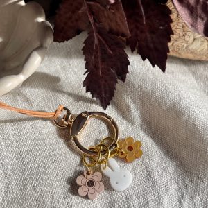 Colorful charm keychain with flower and bunny charms, on beige fabric with dark purple leaves.