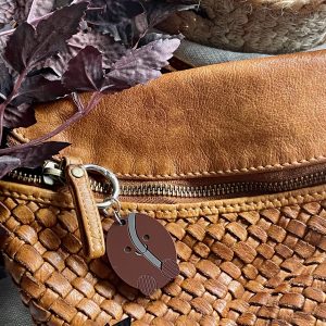 Soft woven brown basket with leather accents and a keychain, styled with purple foliage. Ideal for home decor and craft projects.