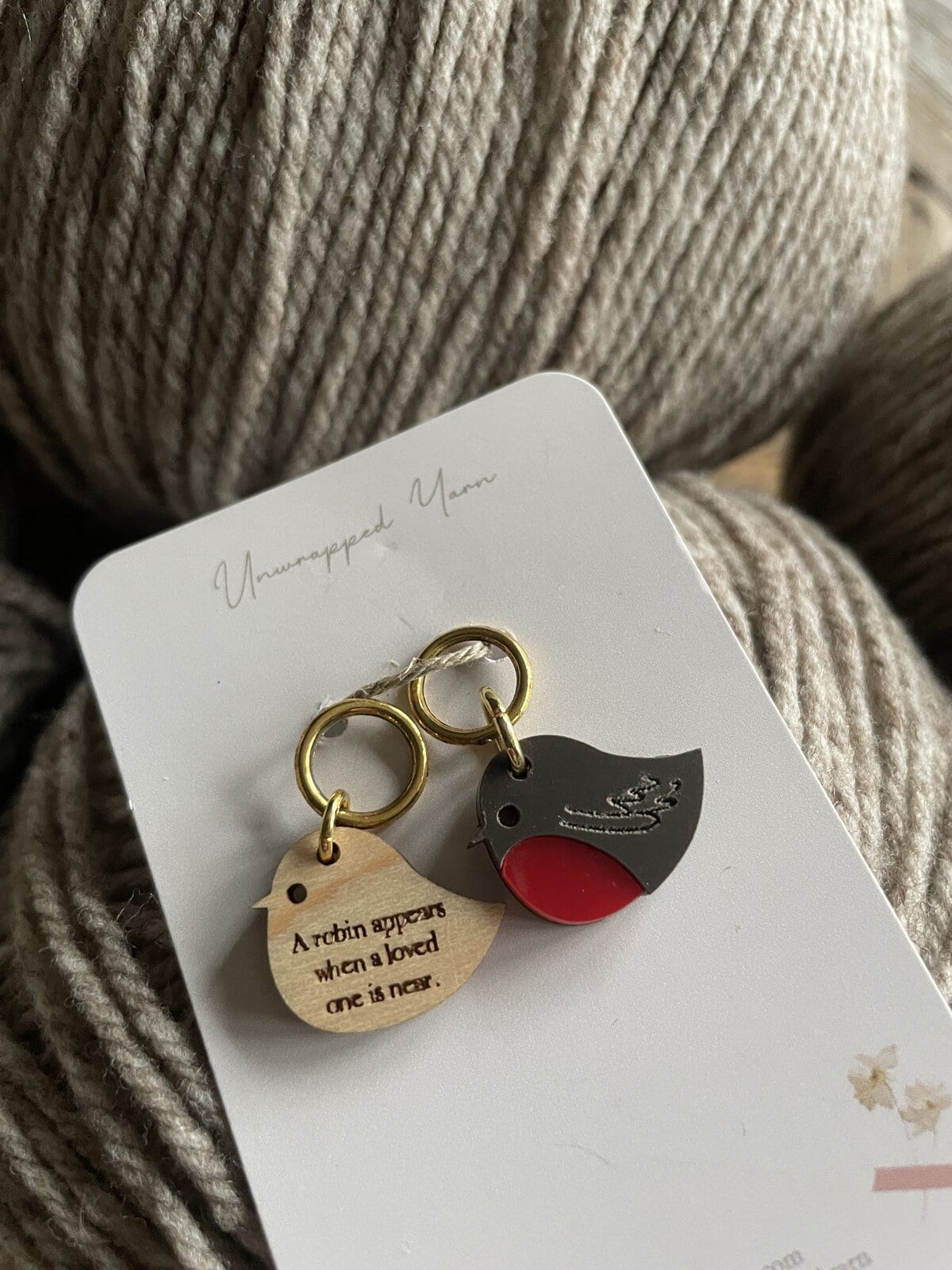 Soft beige yarn with metallic bird-themed enamel charms on Unwrapped Yarn packaging, perfect for knitting or crocheting projects.