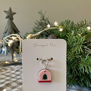 Festive holiday tree ornament with a green Christmas tree charm on a pink background, ideal for Christmas decor.