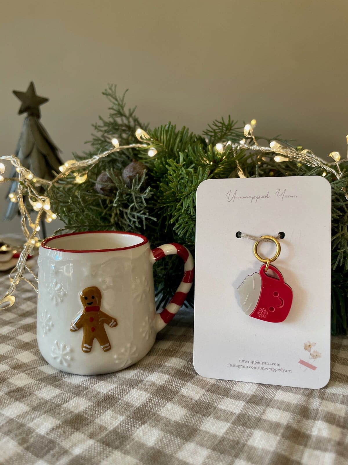 Cozy holiday mug with gingerbread charm next to Christmas greenery and fairy lights, perfect for festive knitting or gift-giving.