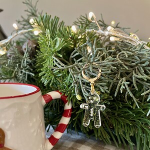 Colorful holiday yarn gingerbread man ornament hanging from festive greenery with a mug nearby.
