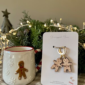 Cozy holiday decor with wooden gingerbread earrings and festive mug on checkered tablecloth.