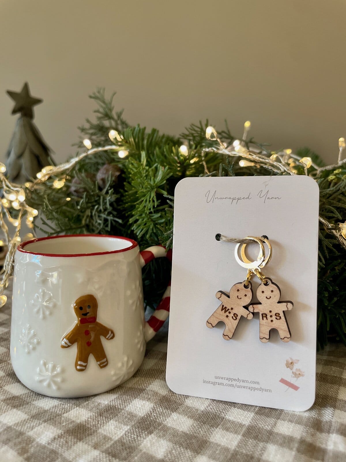 Cozy holiday decor with wooden gingerbread earrings and festive mug on checkered tablecloth.