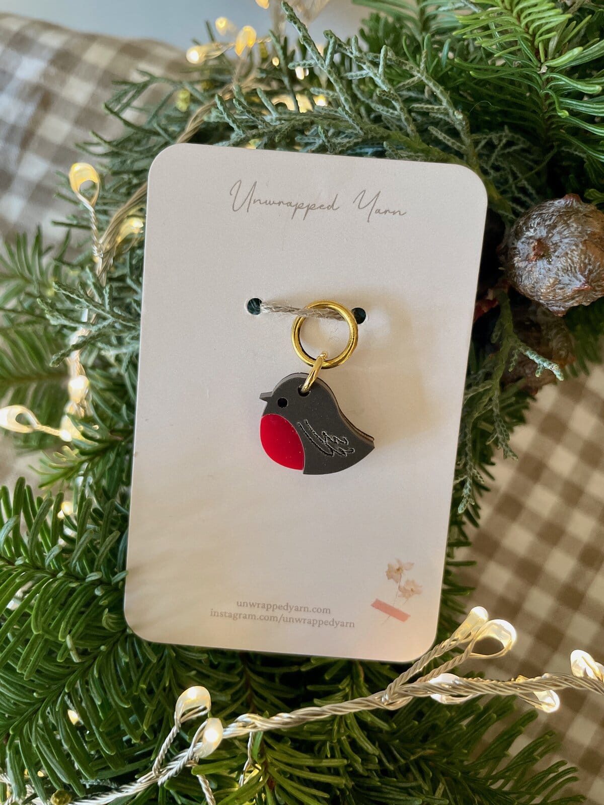 Colorful bird-shaped resin keychain, on a white card, surrounded by green foliage and fairy lights.