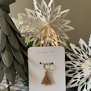 Delicate gold tree-shaped holiday ornament on white card with "Unwrapped Yarn" branding and festive decor background.