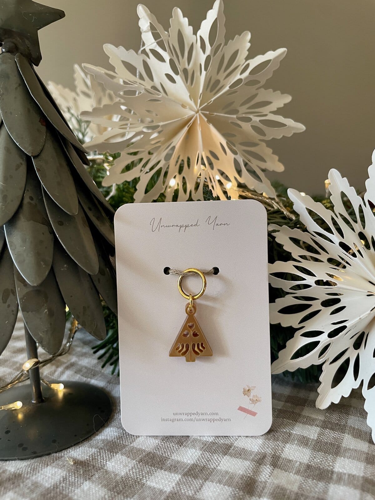 Delicate gold tree-shaped holiday ornament on white card with "Unwrapped Yarn" branding and festive decor background.