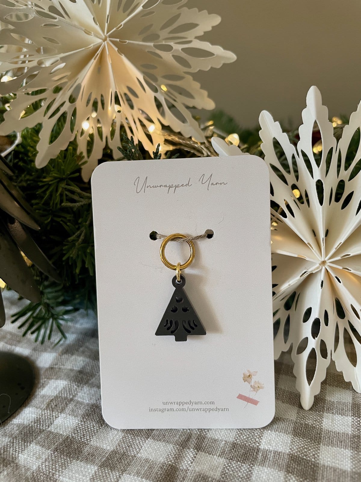 Small black Christmas tree keychain with gold ring on white display card.