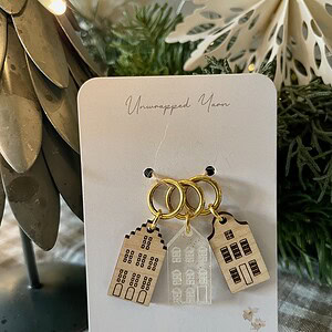 Delicate house-shaped earrings on a jewelry card, featuring gold hoops and layered building designs.
