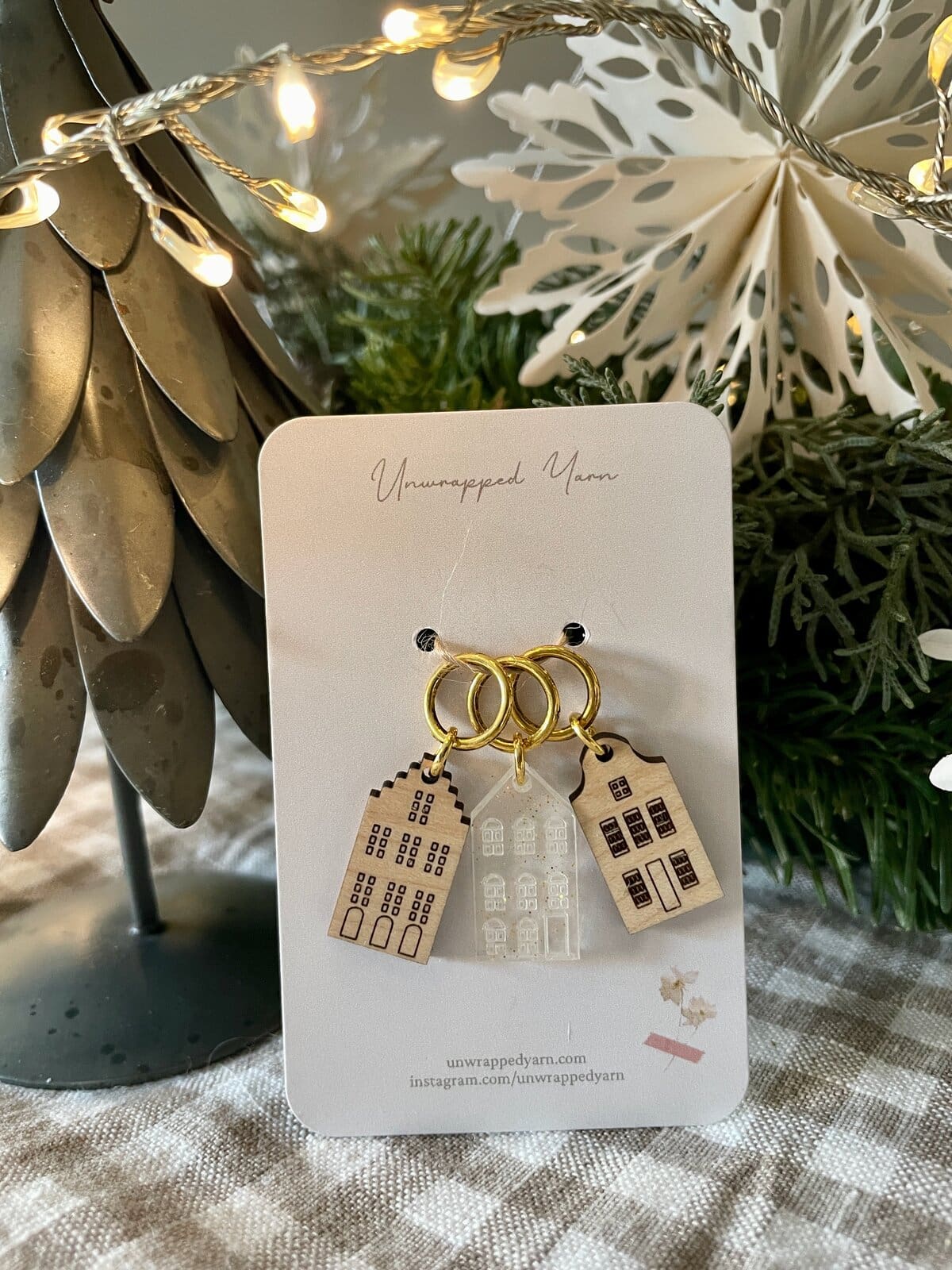 Colorful cityscape keychain charms on gold rings under warm fairy lights and holiday decor.