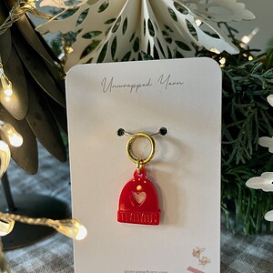 Red heart-shaped jewelry charm with a gold hoop, displayed on a white Unwrapped Yarn card.