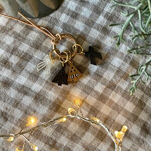 Chic keychain with holiday tree charms on checkered fabric, surrounded by greenery and warm fairy lights.