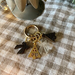 Colorful holiday-themed acrylic keychain charms on gold rings, laid on checkered fabric next to faux plant.