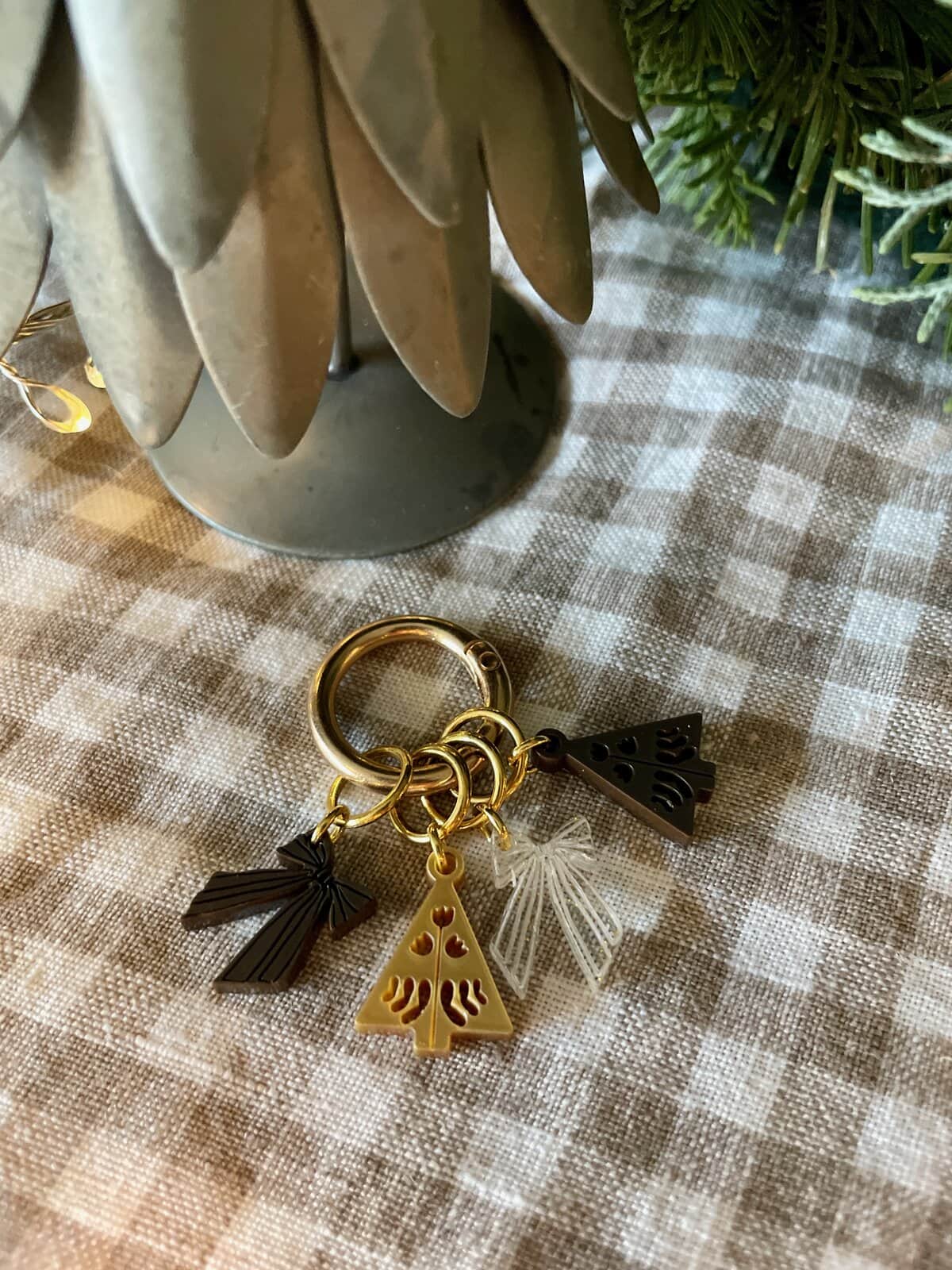 Colorful holiday-themed acrylic keychain charms on gold rings, laid on checkered fabric next to faux plant.