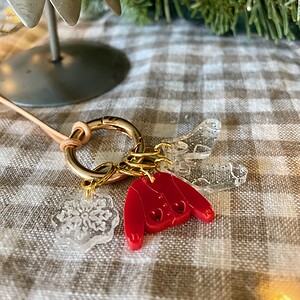 Colorful crochet hook keychain with clear snowflake and heart charms on checkered tablecloth, ideal for crochet enthusiasts.