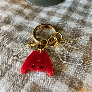 Colorful holiday-themed acrylic keychain with snowflake and mitten charms on checkered fabric.