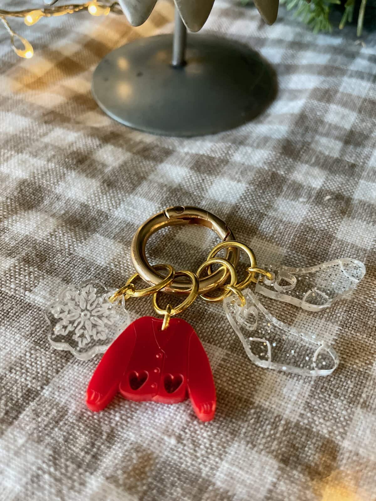 Colorful holiday-themed acrylic keychain with snowflake and mitten charms on checkered fabric.
