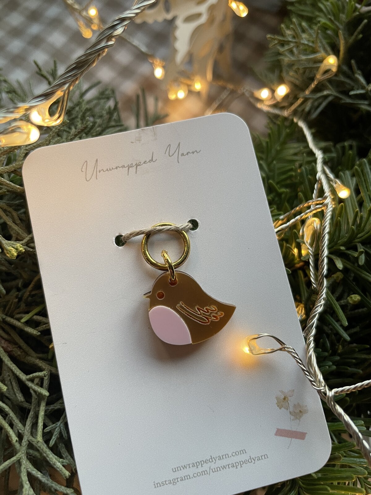 Colorful bird enamel keychain on white card with natural and warm festive lighting.