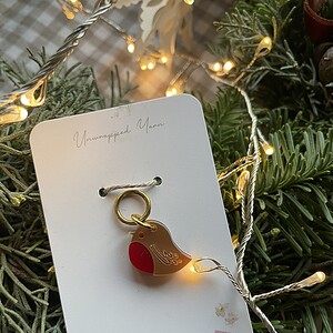Colorful bird-shaped yarn charm on a white display card with Christmas lights and greenery.