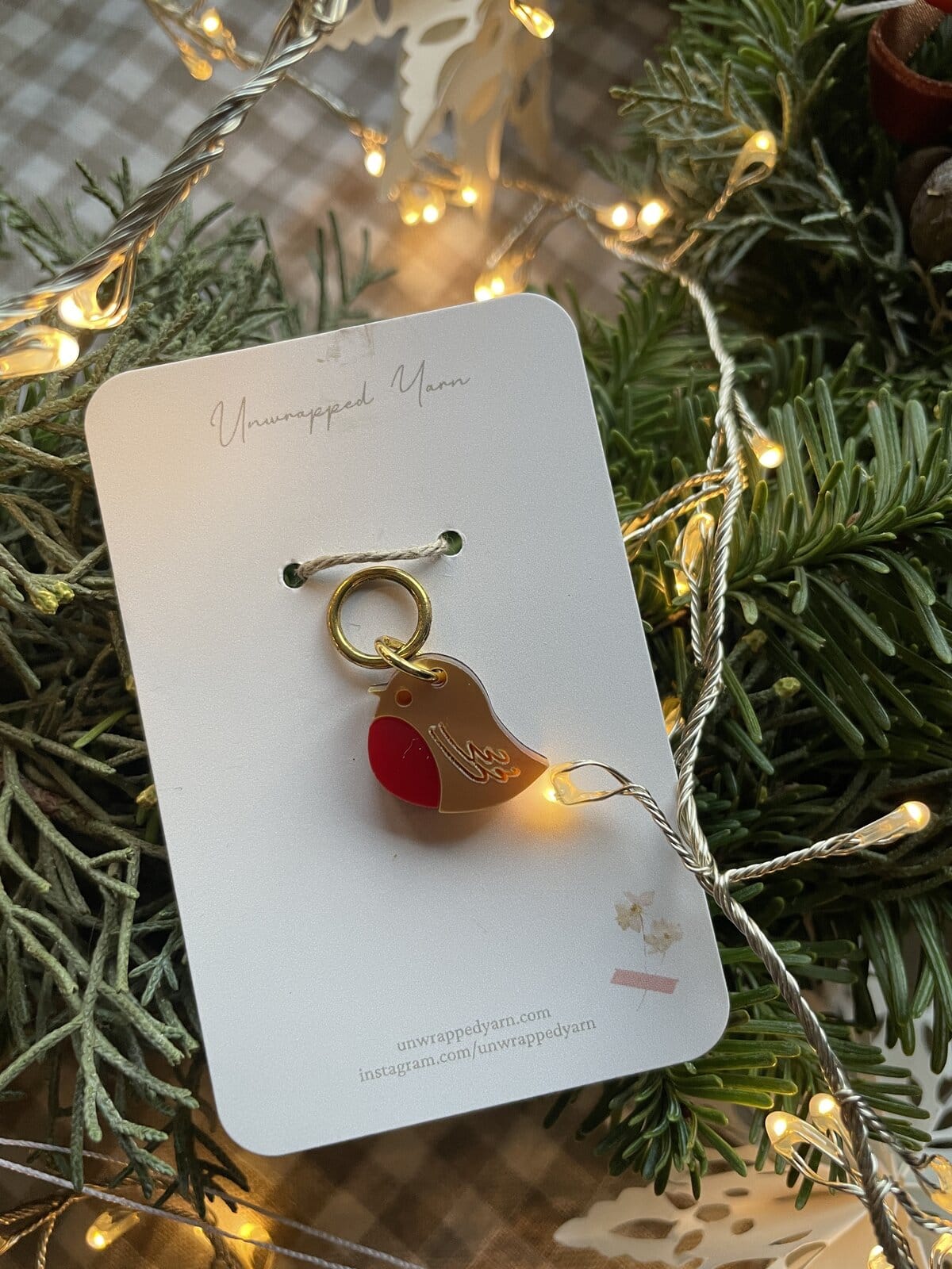 Colorful bird-shaped yarn charm on a white display card with Christmas lights and greenery.
