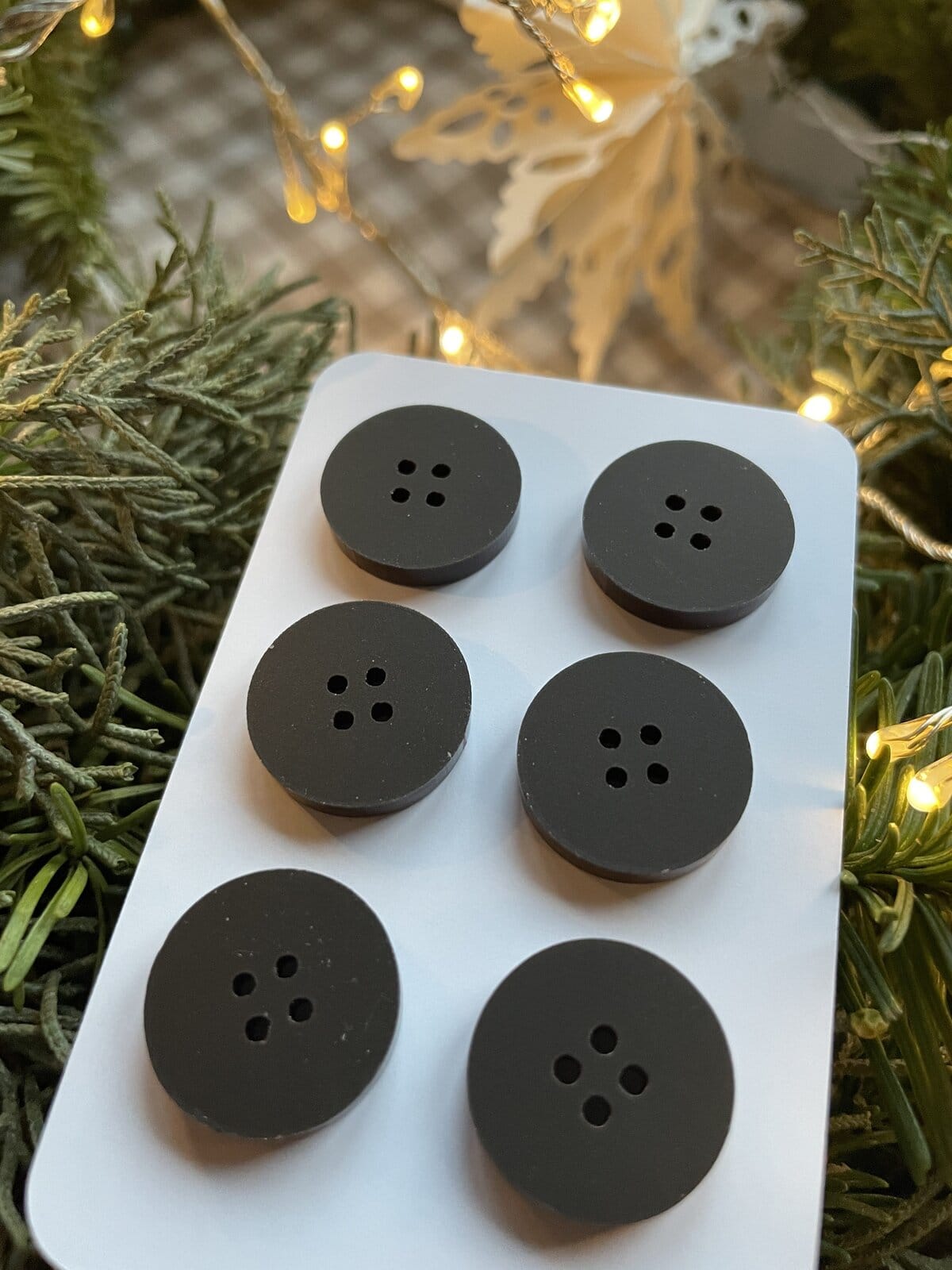 Black round buttons with four-hole design, ideal for knitting and crochet projects, displayed on a white card.