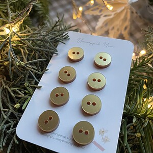 Clothing buttons displayed on a card with a Christmas decor background and warm string lights.