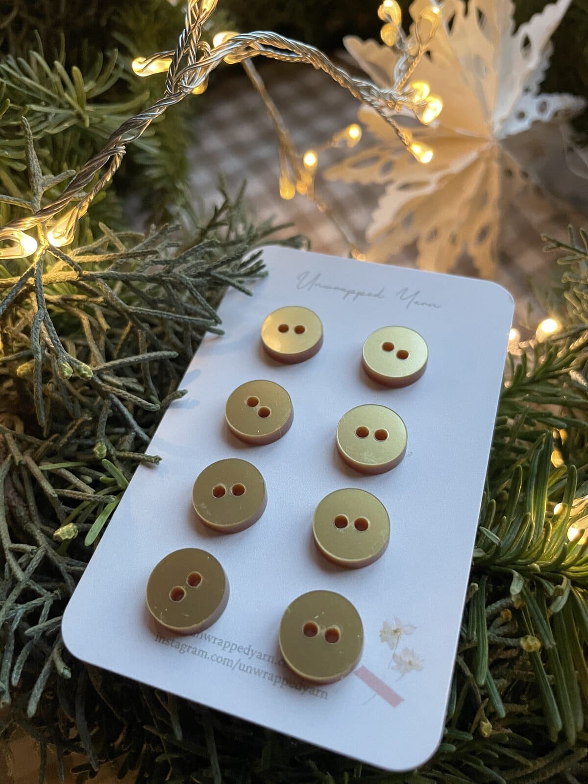 Clothing buttons displayed on a card with a Christmas decor background and warm string lights.